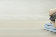 Stack of cashmere clothes on wooden table, space for text. Banner design